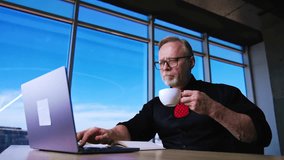 Caucasian businessman working on laptop and drinking coffee. Low angle view on the man having coffee break at workplace.