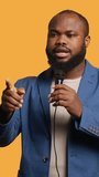 Vertical video African american motivational speaker holding monologue using microphone, gesturing with hands, studio background. Energetic BIPOC speaker talking during presentation using mic, doing