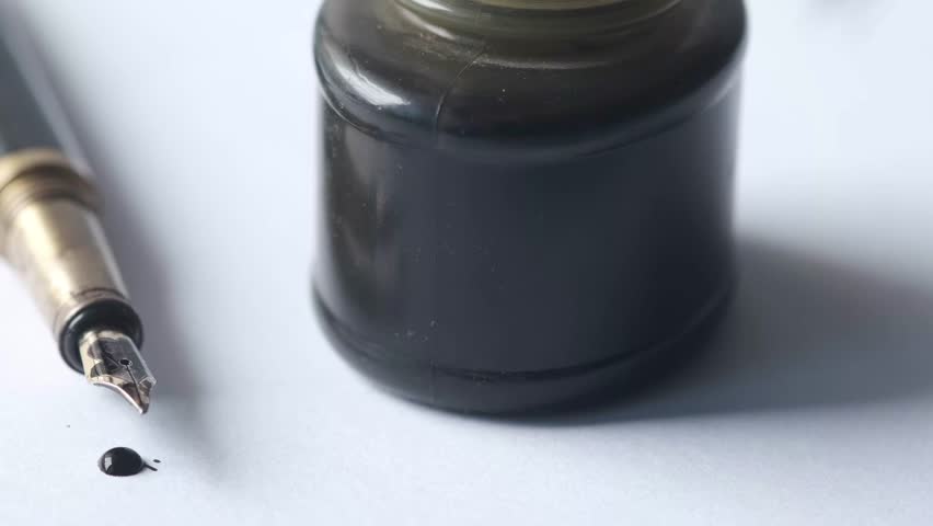 Macro shot of a fountain pen tip and ink bottle on paper, a single drop of ink visible Royalty-Free Stock Footage #3482919939