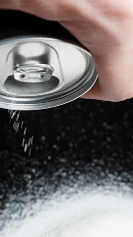 Vertical video. Pure white sugar being poured from a soda can onto a black table by a man. Concept of harmful drinks.