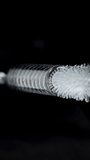 Vertical video. The brush for cleaning straws with a flexible metal handle enters the inside of the tube and rotates. Close-up on a black background.