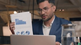 Smiling man Indian Arabian businessman guy male consultant manager business coach talk discuss online consultation video call on laptop showing papers diagram sales charts graphs analyzing at office - Powered by Shutterstock - Get 15% off with code: PIKWIZARD15