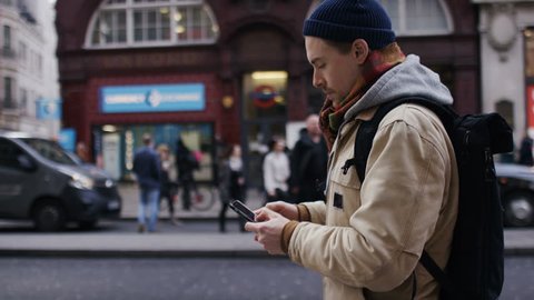 Young man using his phone as he walks on the high street, in slow motion