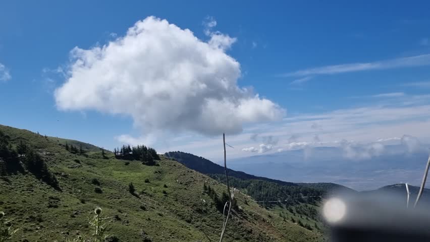 Majestic clouds gracefully hover above the rugged Algerian mountains, casting a picturesque backdrop against the vast blue sky