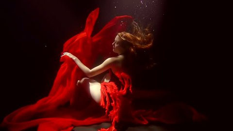 A young woman with red hair dances deep in the sea waters, the fabric flutters
