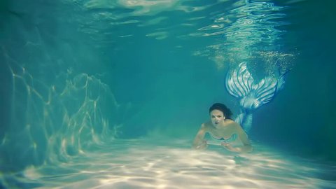 a woman swims in the pool, a lady dives under the water with a fish tail, she swims into the depths