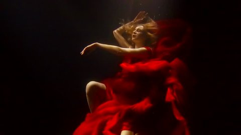 a woman with red hair dances under the water, a lady dressed in a lush red dress, she dances and turns