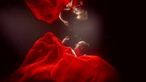 a young woman in a lush red dress swims under the water, she touches the reflection