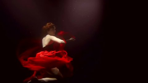 a young woman in a lush red dress turns to the side under the water, we see her legs