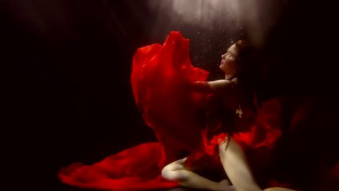 young woman in lush red dress dancing under water, lady looking up, there is light