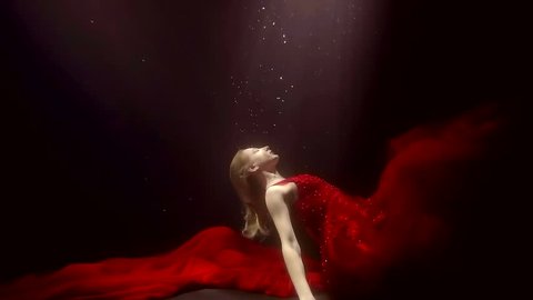 a young woman in a lush red dress rises up from the seabed, she drops her hands down