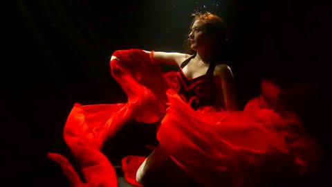 a woman with red hair is under water, a lady dressed in a lush red dress, she raises her hand up
