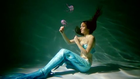 The mermaid crouched in the water, the woman tries to touch the sea jellyfish that float near the lady
