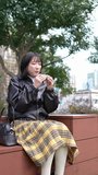 Vertical video of a young Japanese woman in her 20s sitting and eating churros in a park around Gotanda Station, Shinagawa-ku, Tokyo in winter 