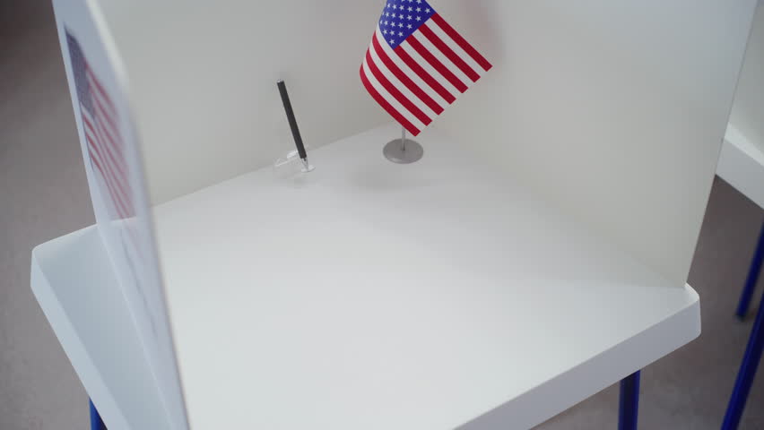 African American male voter comes to voting booth at polling station, makes choice and fills out paper ballot. US citizen during National Elections Day in the United States of America. Civic duty.