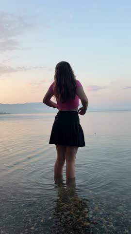 silhouette of young slender girl in water clear water against horizon girl dancing having fun. teenager young woman with hair big pebbles in water blue sky early morning travel photo shoot