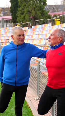 Smiling old sportive friends warming up in an outdoor field before start to run together