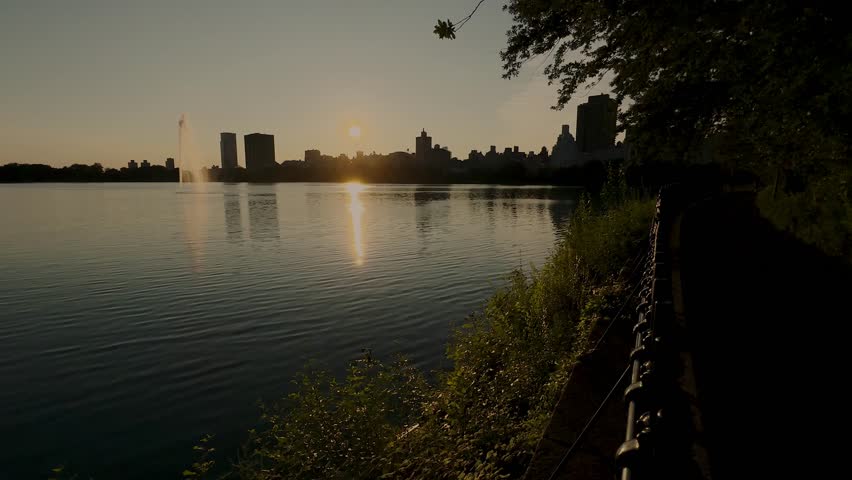 Sunrise from the Jacqueline Kennedy Onassis Reservoir in Central Park, New York. Lake surrounded by New York skyscrapers with reflections on the lake in summer.