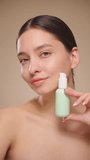 Portrait young woman uses creams of her face. Concept for fresh moisturized skin beautiful closeup cosmetic face happy healthy model.   Model with a bottle of face cream. Slow motion, vertical video