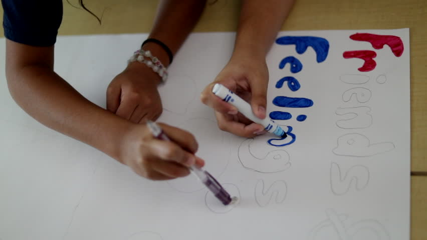 This slow motion clip shows a group of 4 students working collaboratively to complete a chart for a later presentation. The focus is on the slow motion movement of hands erasing, tracing, and pointing