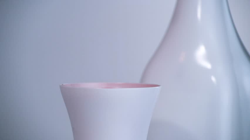 Red drop slowly falls into a white cup. Static view of the quiescent surface response after impact