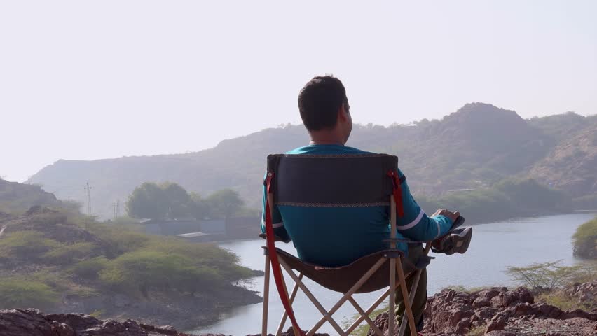 isolated man sitting at camping chair at mountain top with lake view at morning