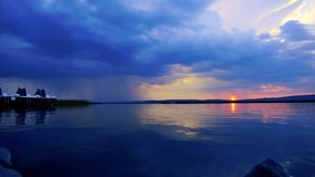 Time lapse footage over the lake in beautiful natural environment during sunset and cloud rainy sky in the background. 