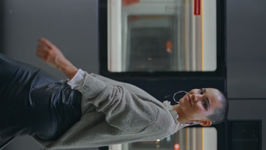 Happy voyager walking platform near high-speed train. Confident short hair woman carrying luggage arrived to destination vertical view. Smiling young girl hipster going railway station looking camera.