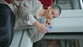 Train passenger video calling by smartphone sitting wagon. Happy short hair woman smiling talking to cellphone camera vertical shot. Cute cheerful girl enjoy online phone conference awaiting departure