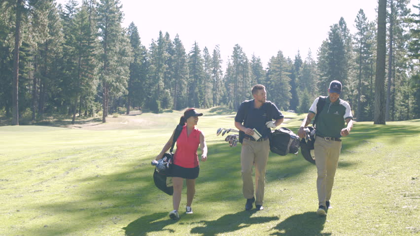 Three people walking on a golf course carrying golf bags