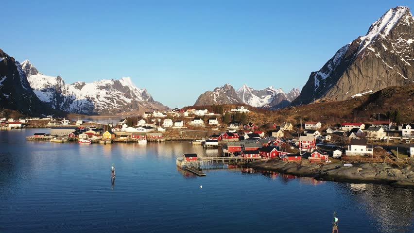 Aerial view of snowy mountains at sunset in Lofoten Islands, Norway. Winter landscape with beautiful road, water, rocks in snow, sky, fjord with pink clouds. Top view from drone.