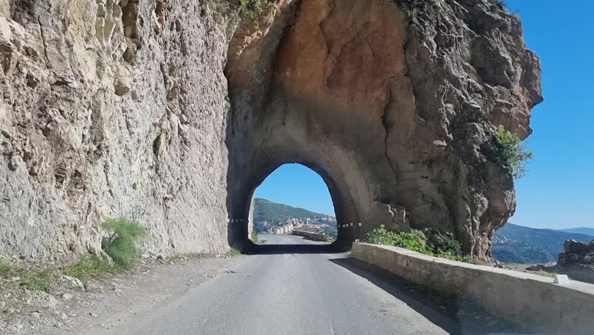 An enchanting journey awaits as you enter the tunnel, leading you to the serene beauty of the Algerian road with majestic mountains in the distance
