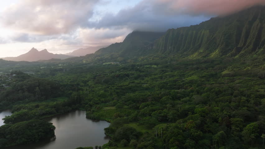 Breathtaking volcano mountain ridge covered by cinematic pink blue rain clouds at sunrise. Scenic nature landscape of Hawaii island. Epic Oahu nature with steep green cliffs at impressive sunrise 4K