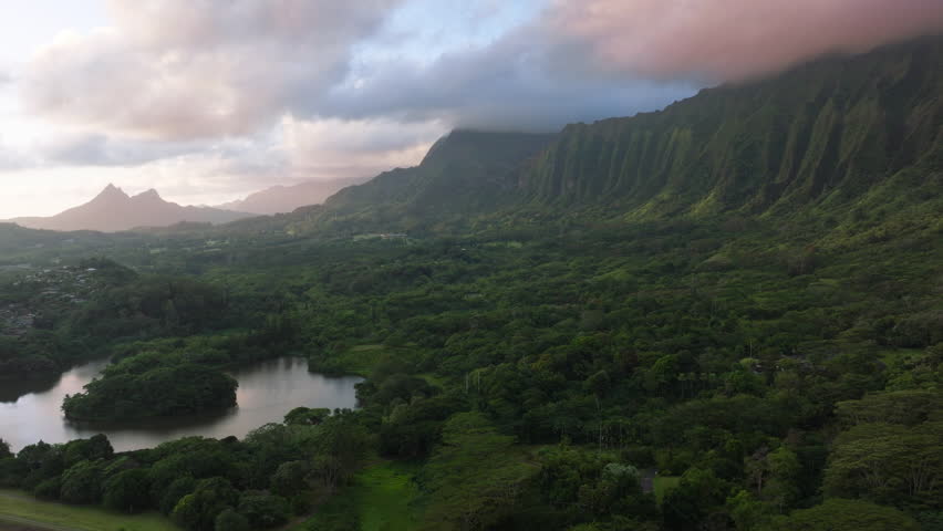 Breathtaking volcano mountain ridge covered by cinematic pink blue rain clouds at sunrise. Scenic nature landscape of Hawaii island. Epic Oahu nature with steep green cliffs at impressive sunrise 4K