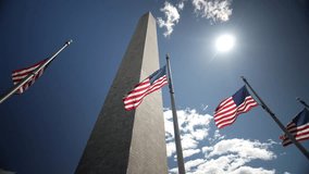 American flags flying at the base of the Washington Monument in Washington, DC, USA, camera looking up into the sun with blue sky moving around the monument. - Powered by Shutterstock - Get 15% off with code: PIKWIZARD15