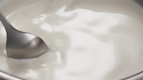 Slow motion closeup stirring liquid cream in stainless steel bowl