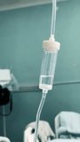 Drip chamber of an intravenous line hung on a stand with blurred patient beds in a hospital ward setting in the background. Close-up shot. Vertically framed video