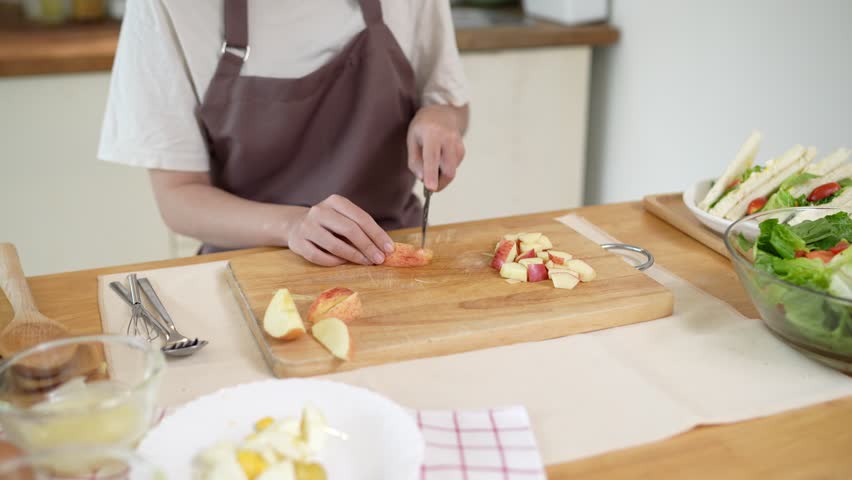 The Asian woman is slicing apples to make a vegetable salad in her home kitchen. 