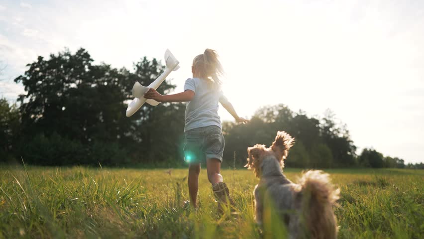 Child with airplane toy dog in tow embodies youthful dream. Excited child pilot toy airplane dog companion in sunny field. Child joy flying toy plane playful dog watches on. Happy girl run in park