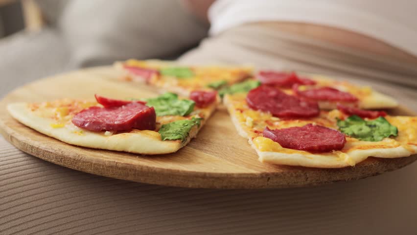Pregnancy fast food. Close up view of young unrecognizable pregnant woman holding plate with tasty pizza enjoying unhealthy nutrition