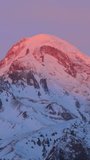 Stepantsminda, Gergeti, Georgia. Mount Kazbek Covered Snow In Winter Sunrise. Morning Dawn Colored Top Of Mountain In Pink-orange Colors. Awesome Winter Georgian Nature Landscape. Vertical Footage.
