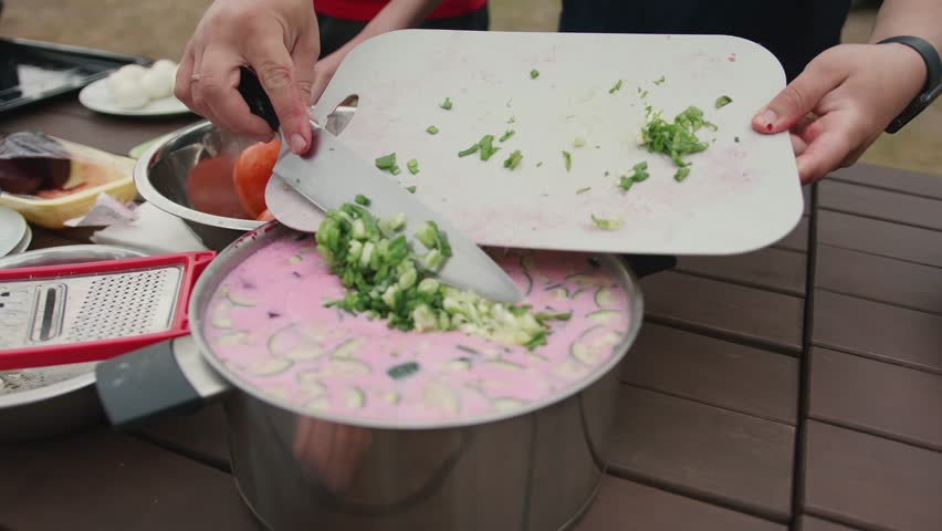 Man pours chopped green onions into cold beet soup. Slow motion. Simple and healthy dish of vegetables that is refreshing in hot summer day