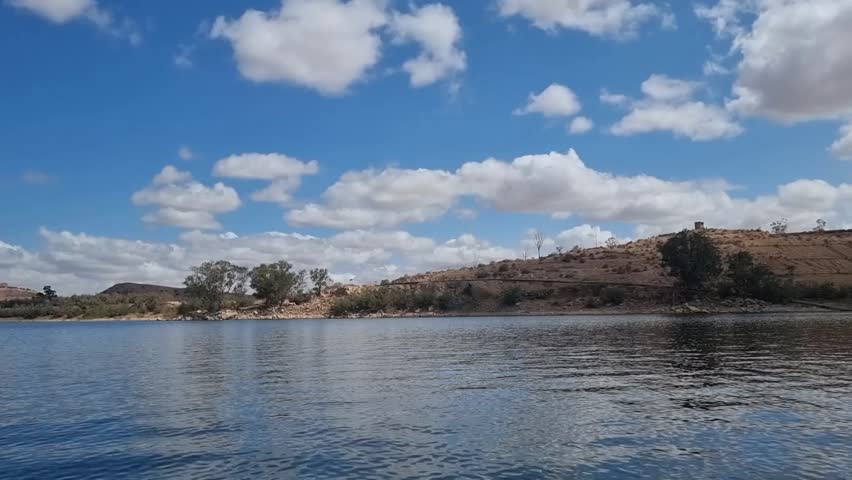 Serene moments on the tranquil waters of an Algerian lake, with a charming boat gently gliding by, framed by a picturesque hill in the background, Algeria