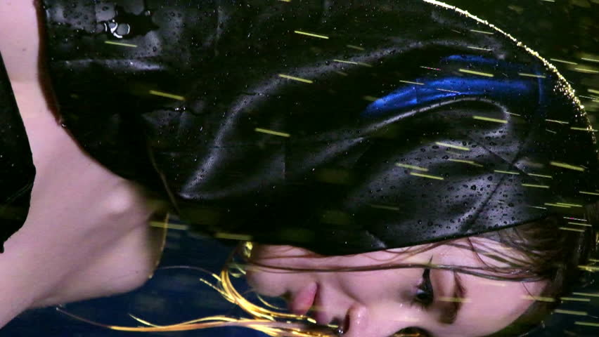 Woman with plump lips adjusts edge of braid standing in rain. Side perspective of lady with shoulders uncovered in torrential downpour