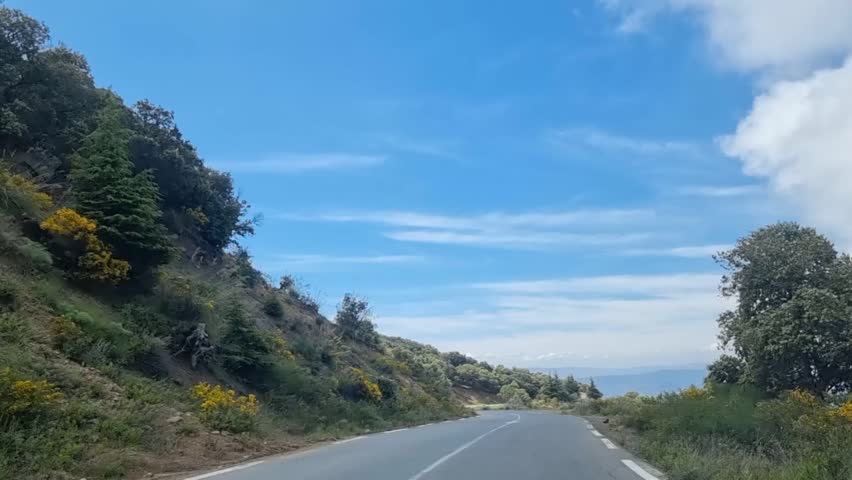 As the winding road gently weaves through the majestic Algerian mountains, the dramatic clouds in the sky create a breathtaking backdrop for a scenic journey