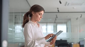 Smiling mid aged mature professional business woman banking manager, 40s female executive or entrepreneur holding fintech tab digital tablet standing in office at work, looking at pad. - Powered by Shutterstock - Get 15% off with code: PIKWIZARD15
