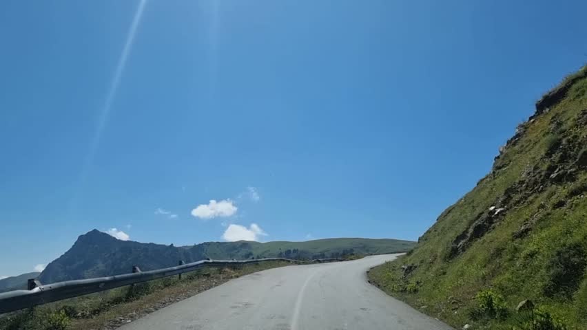 As the winding road gently weaves through the majestic Algerian mountains, the dramatic clouds in the sky create a breathtaking backdrop for a scenic journey