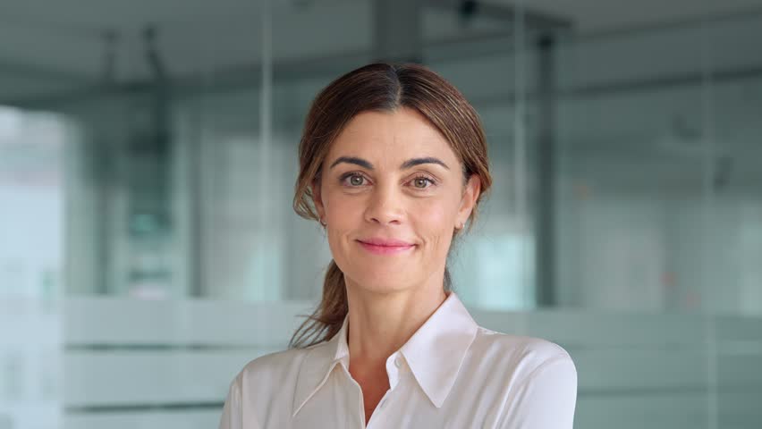 Happy 45 years old Latin professional middle aged business woman corporate leader, smiling positive mature female executive manager standing in office looking at camera, face portrait.