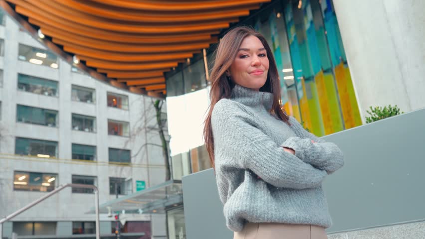 Young smiling professional business woman, happy confident 30s lady student standing outdoors on big city street business district, looking at camera, crossing arms, portrait.