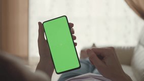 Woman Lying on Couch Using Smartphone With Chroma Key Green Screen Scrolling Through Social Media. Girl Mobile Phone Using Green Screen Female Using Smartphone Browsing Internet Watching Video Content
